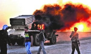Rebeldes pasan junto a un incendiado camión lanzamisiles de las fuerzas de Gadafi cerca de los pozos petroleros de Ras Lanuf. ::
AFP/